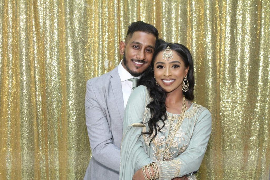 Bride and groom posing in a Fun Snaps photo booth with a gold sequin backdrop at their wedding near Mississauga